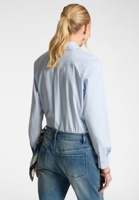 Camicia blu chiaro con bottoni, dalla vestibilità rilassata, maniche lunghe e una texture morbida, abbinata a jeans in denim di lavaggio medio. Look casual.