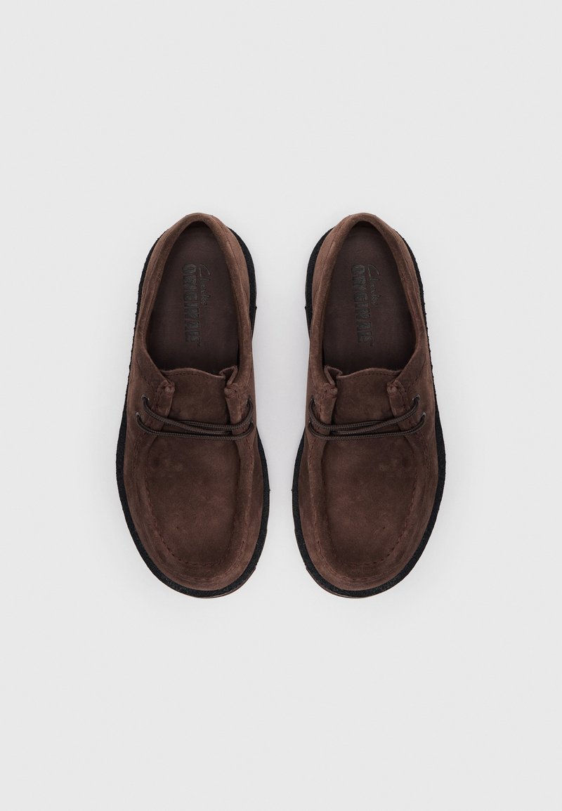 Bruine suède schoenen met een ronde vorm, zwarte rubberen zolen en decoratieve veters. De binnenzool heeft een reliëfdruk.