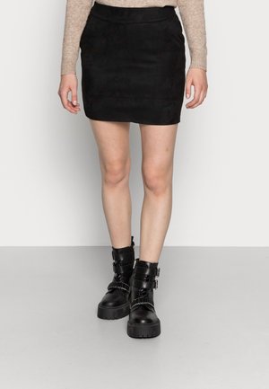 Jupes mini en daim noir avec une texture lisse, assortie à des bottines noires à la cheville avec des sangles et des accents métalliques, sur un fond neutre.