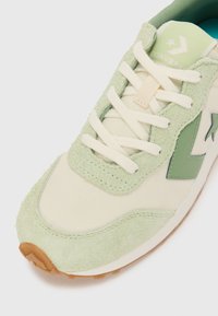 Lys grønn semsket lær og kremfarget stoff sneakers med hvite lisser, utstyrt med en grønn stjerne-logo og en teksturert gummisåle. Minimalistisk design.
