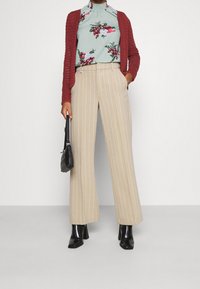 Beige stribede vide ben bukser parret med en blomsterbluse i teal og en rød strik cardigan. Accessories inkluderer en lille sort håndtaske.