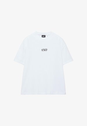 Fehér rövid ujjú, kerek nyakú póló, a mellkas közepén fekete "STWD" felirattal, és a galléron egy kis fekete márkajellel.