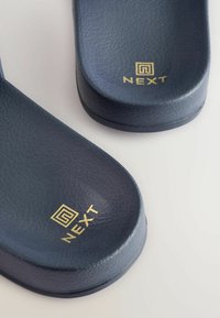 Infradito blu texturizzati con una superficie liscia, dotati di un logo dorato "NEXT". I bordi sono arrotondati e la suola è piatta.