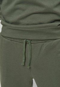 Mørkegrønne joggebukser med snøring i midjen, glatt tekstur, elastiske mansjetter og et enkelt design uten synlige mønstre.