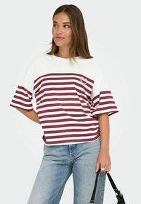 Gestreept T-shirt met een wit en bordeauxrood design. Kenmerkt zich door een hartvormige versiering en losse korte mouwen. Combinatie met lichtblauwe denim.