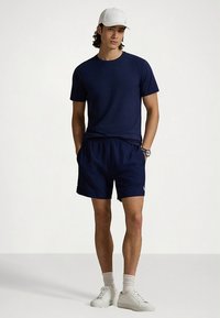 Marineblå t-skjorte og matchende shorts, begge laget av lett stoff. Hvit caps, hvite joggesko og ribbestrikkede ankelsokker fullfører antrekket.