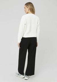 Pull en tricot blanc avec un col rond, associé à un pantalon large noir ; des baskets argentées complètent la tenue.