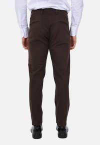 Chino marroni con una texture liscia, taglio slim e due tasche posteriori. Indossati con scarpe nere lucide.