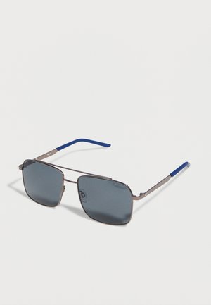 Gafas de sol de forma cuadrada con lentes gris oscuro, montura metálica plateada fina y puntas de varilla recubiertas de azul.
