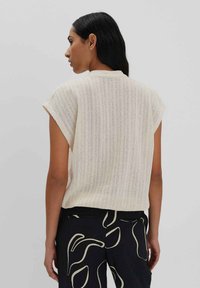 Licht crèmekleurig gebreid T-shirt met korte mouwen, voorzien van een ribbelstructuur en een relaxte pasvorm, gecombineerd met zwarte broek met een abstract crèmekleurig patroon.