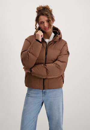 Bruine pufferjas met een capuchon, voorzien van een rits aan de voorkant en ribgebreide manchetten, gecombineerd met lichtblauwe jeans. Glad oppervlak en gestikte details.