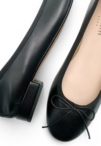 Ballerine in pelle nera con punta arrotondata, tacco basso e un dettaglio a fiocco nella parte anteriore. Struttura liscia con una leggera lucentezza.