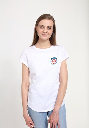 Biała bawełniana koszulka z krótkimi, podwiniętymi rękawami, z niebiesko-czerwonym okrągłym logo "SPIDEY" na piersi. W połączeniu z jasnoniebieskimi dżinsami.