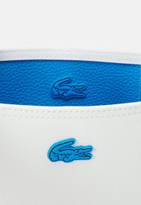 Logo de crocodile bleu embossé sur tissu blanc avec une bande de fond texturée bleue au-dessus.