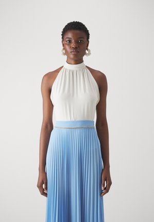Haut à col halter en tissu blanc cassé associé à une jupe fluide plissée de couleur bleu clair ; présente une ceinture ornée de bijoux.