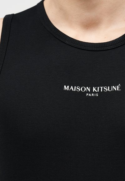 Gros plan d'une personne portant un débardeur côtelé noir avec le texte blanc « MAISON KITSUNÉ PARIS » sur la partie supérieure de la poitrine.