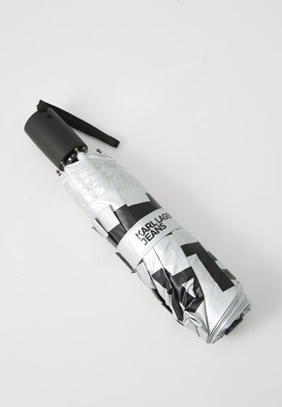 Parapluie compact argenté avec motif géométrique noir, doté d'une poignée noire et d'une sangle. Comprend le logo "KARL LAGER JEANS".