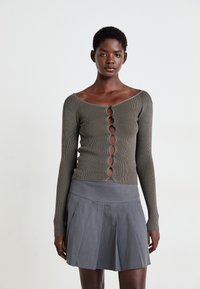 Olivegrünes, geripptes Langarmoberteil mit sechs Knopfverschlüssen und schulterfreiem Design, kombiniert mit einem grauen, ausgestellten Plisseerock.