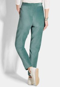 Groene corduroy broek met een slim fit ontwerp, elastische tailleband, zijzakken en een gestructureerde afwerking, gedragen met lichtgekleurde sneakers.