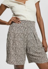 Pantaloni corti a vita alta con un motivo floreale nero e beige, caratterizzati da pieghe, un tessuto testurizzato e una cintura elastica per il comfort.