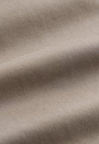 Gros plan d'un tissu sergé beige montrant une texture côtelée diagonale et des plis lisses.