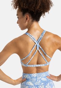 Brassiere sportivo di colore azzurro chiaro con un motivo floreale; presenta sottili spalline incrociate sul retro e un tessuto liscio e elasticizzato.