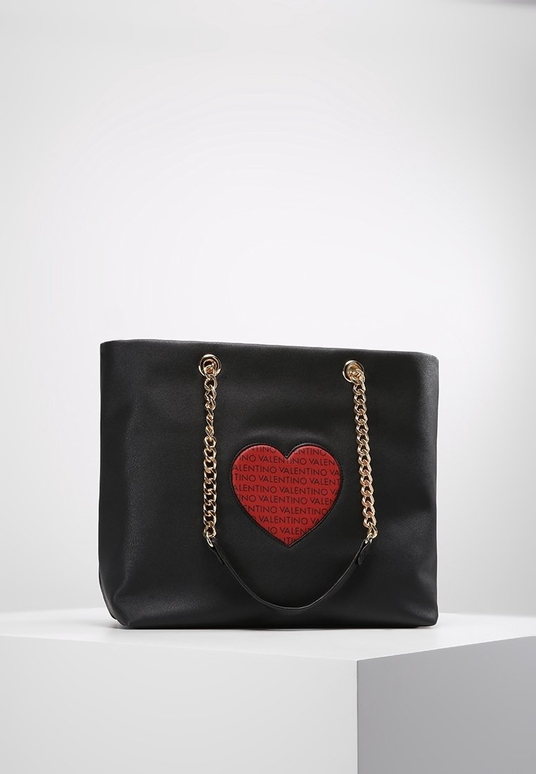 Svart Valentino tote-väska med gyllene kedjehandtag och ett röd hjärtat tryckt upprepade gånger med "VALENTINO."