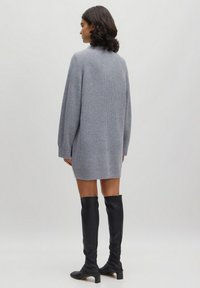 Grijze geribbelde trui jurk met lange mouwen, knielang, gecombineerd met zwarte laarzen tot boven de knie met een blokhak. Soepele textuur.