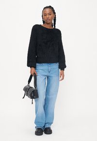 Zwarte fuzzy trui met lange mouwen, lichtblauwe losse jeans en een kleine zwarte crossbody tas, compleet met zwarte platform schoenen.
