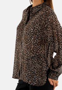 Blusa de leopardo transparente con cuello y mangas largas, con un corte holgado y sutiles aberturas laterales en el dobladillo.