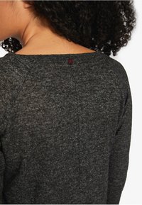 Grau gestricktes Oberteil mit Rundhalsausschnitt und Raglanärmeln. Auffälliges Detail: Ein kleiner roter Knopf am Rücken, strukturierte Stoffoberfläche.