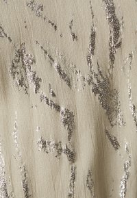Teksturert stoff i beige med metallisk sølvstriper. Overflaten har et mykt, litt krøllete utseende med glitrende detaljer.