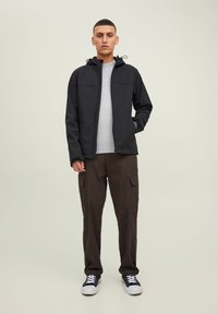 Chaqueta negra con cremallera y capucha, con cordones, llevada sobre un suéter texturizado gris claro y pantalones cargo oscuros, acompañada de zapatillas negras.