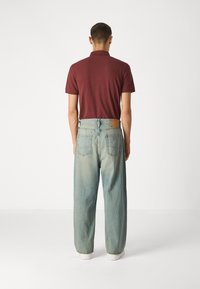 Burgunderfarbendes Poloshirt mit kurzen Ärmeln, kombiniert mit hellblauen, hochtaillierten, weiten Jeans, die zwei Gesäßtaschen und ein hellbraunes Lederetikett haben.