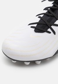 Scarpino da calcio bianco con lacci neri, caratterizzato da una tomaia texturizzata con dettagli dorati e una suola nera. Cinque tacchetti bianchi per la trazione.