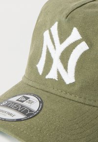 Καπέλο σε ελαιώδες πράσινο με λευκό κεντημένο λογότυπο NY. Διαθέτει κυρτή γείσο και ρυθμιζόμενο λουράκι. Οι ετικέτες περιλαμβάνουν τα "New Era" και "9TWENTY."