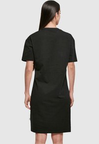 Svart kjole med korte ermer i bomull, med rett snitt, rund halslinning og sømdetalj i livet. Minimalistisk design uten mønstre.