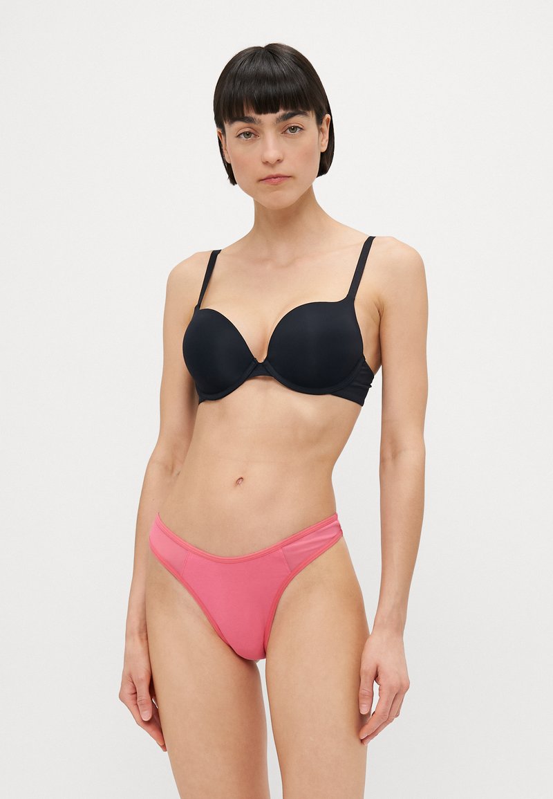 Melnā formēta krūštura kausa ar regulējamiem siksniņām, apvienots ar rozā bikini apakšbiksēm ar minimālistisku dizainu un gludu tekstūru.