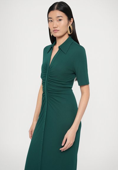 Zelené šaty po kolená s krátkymi rukávmi, nariaseným predným dielom, klasickým golierom a gombíkovými detailmi vpredu. Hladká textúra látky.