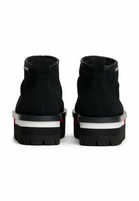 Botas de tobillo de ante negro con un cuello acolchado, que cuentan con una suela de plataforma gruesa en negro, blanco y rojo, y paneles laterales texturizados.