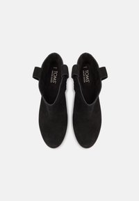 Botas ankle de ante negro con tacón abierto, con un diseño sencillo y un lazo en la parte trasera para una fácil puesta. Marcadas con "TOMS" en el interior.