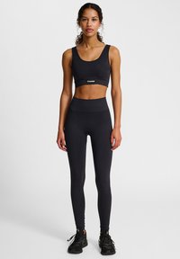 Czarny sportowy krótki top z logo, zestawiony z czarnymi legginsami z wysokim stanem. Gładki, elastyczny materiał o dopasowanym kroju i minimalistycznych akcentach.
