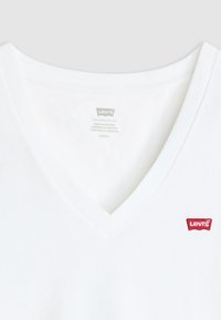 Camiseta branca de algodão com decote em V e patch com o logótipo vermelho da Levi's ao peito, apresentando um design simples e limpo e uma textura suave.
