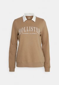 Brun sweatshirt med vit krage, försedd med texten "HOLLISTER SOUTHERN CALIFORNIA" i vitt. Mjuk tyg, ribbade muddar och nederkant.