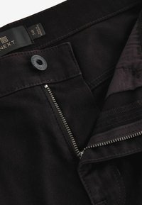 Black cotton fabric pants featuring a zipper fly, button closure, and subtle stitching details. Interior shows contrasting fabric texture.