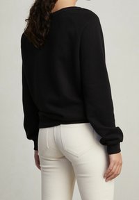 Schwarzer Sweatshirt mit lässigem Schnitt, gerippten Bündchen und Rundhalsausschnitt, kombiniert mit engen weißen Jeans, die über ein Rückentaschendesign verfügen.
