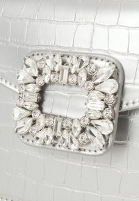 Silver croc-embossed handbag featuring a rectangular rhinestone buckle with various shapes and sizes, adding a sparkling detail.