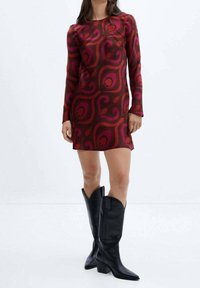 Robe ajustée à manches longues en tissu bordeaux avec des motifs tourbillonnants roses. Associée  à des bottes de cowboy en cuir noir montant jusqu'aux genoux.