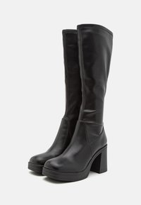 Bottes noires montantes en matériau synthétique lisse, avec un talon épais, un bout rond et des détails de couture minimalistes.