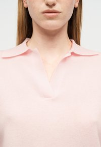Gros plan sur une personne portant une chemise à col rose pâle avec une encolure en V, montrant la partie inférieure du visage et le cou.